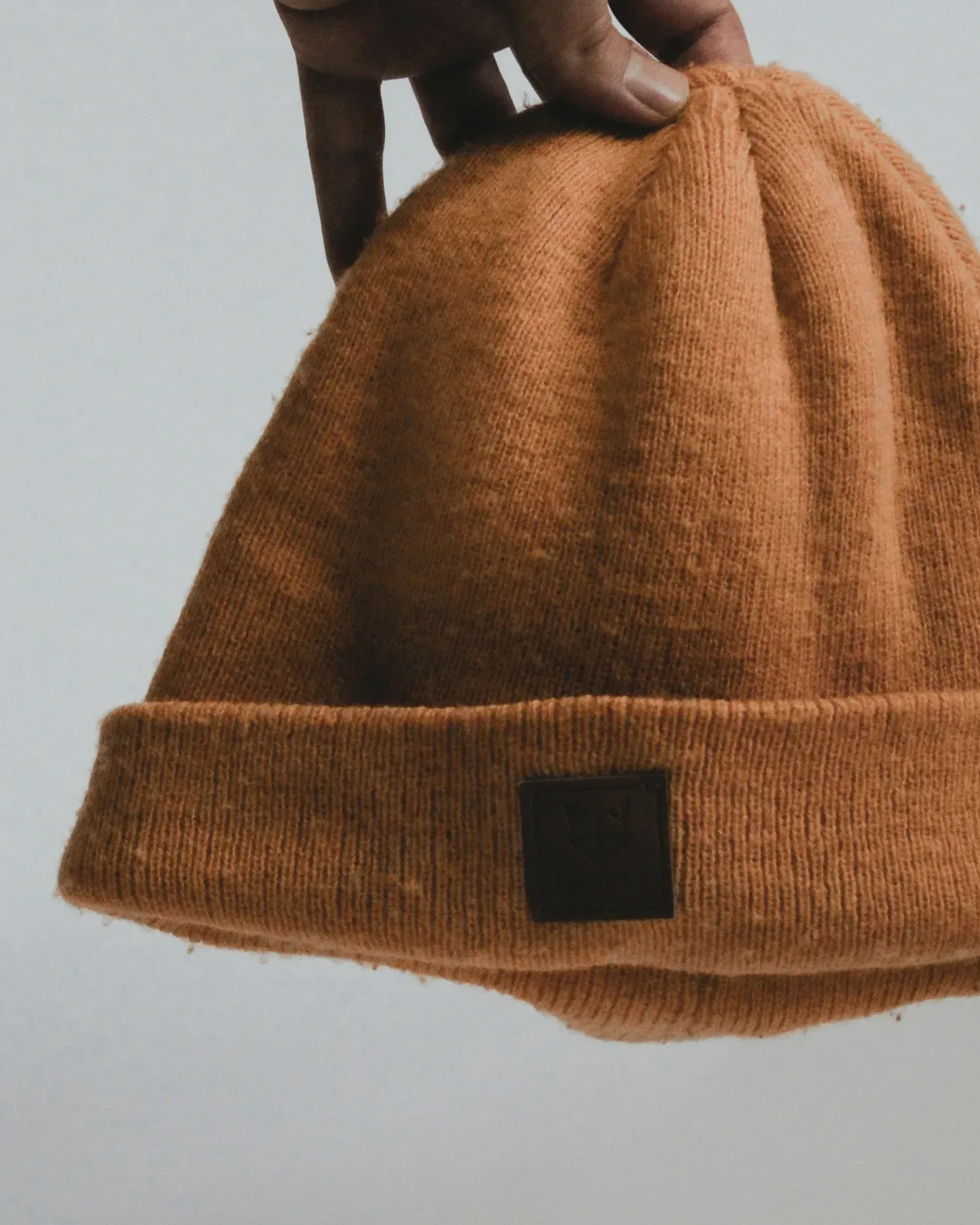 Rostfarbene Strickbeanie mit Umschlag, vor hellgrauem Hintergrund hochgehalten