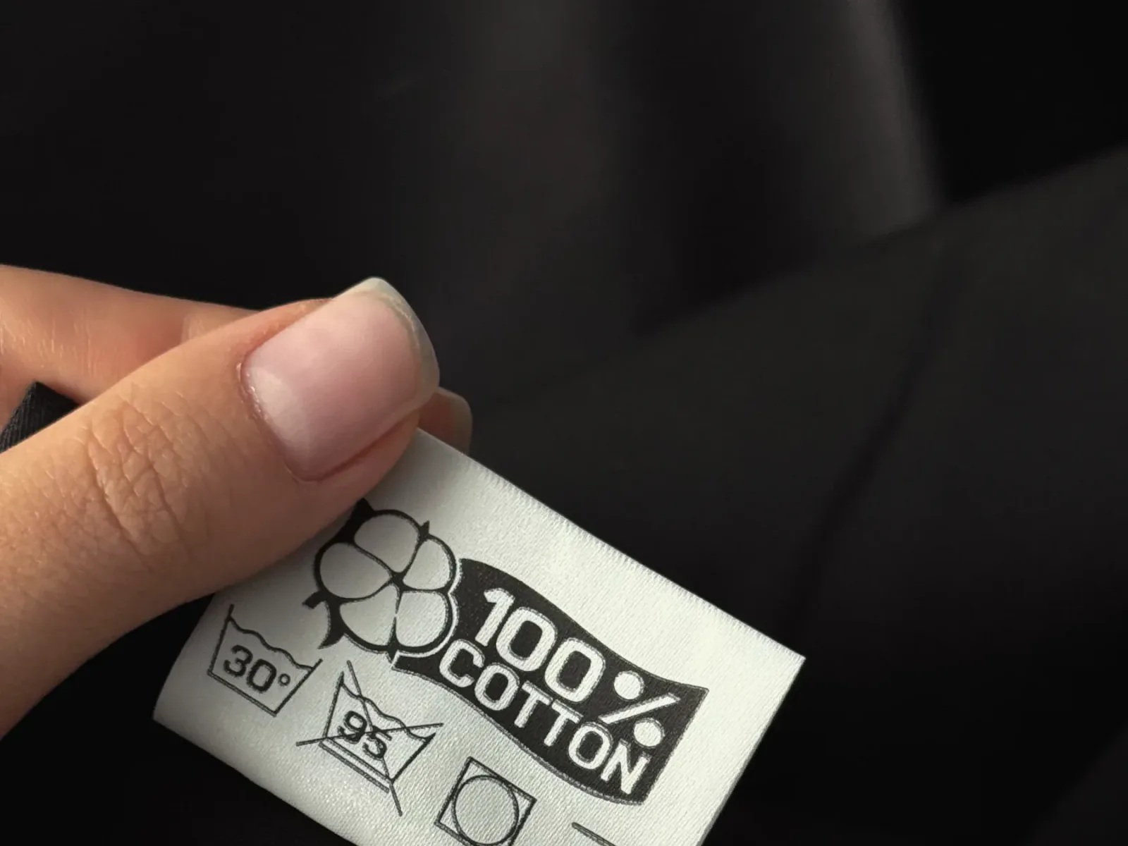 Hands holding a printed care and composition label on a black garment