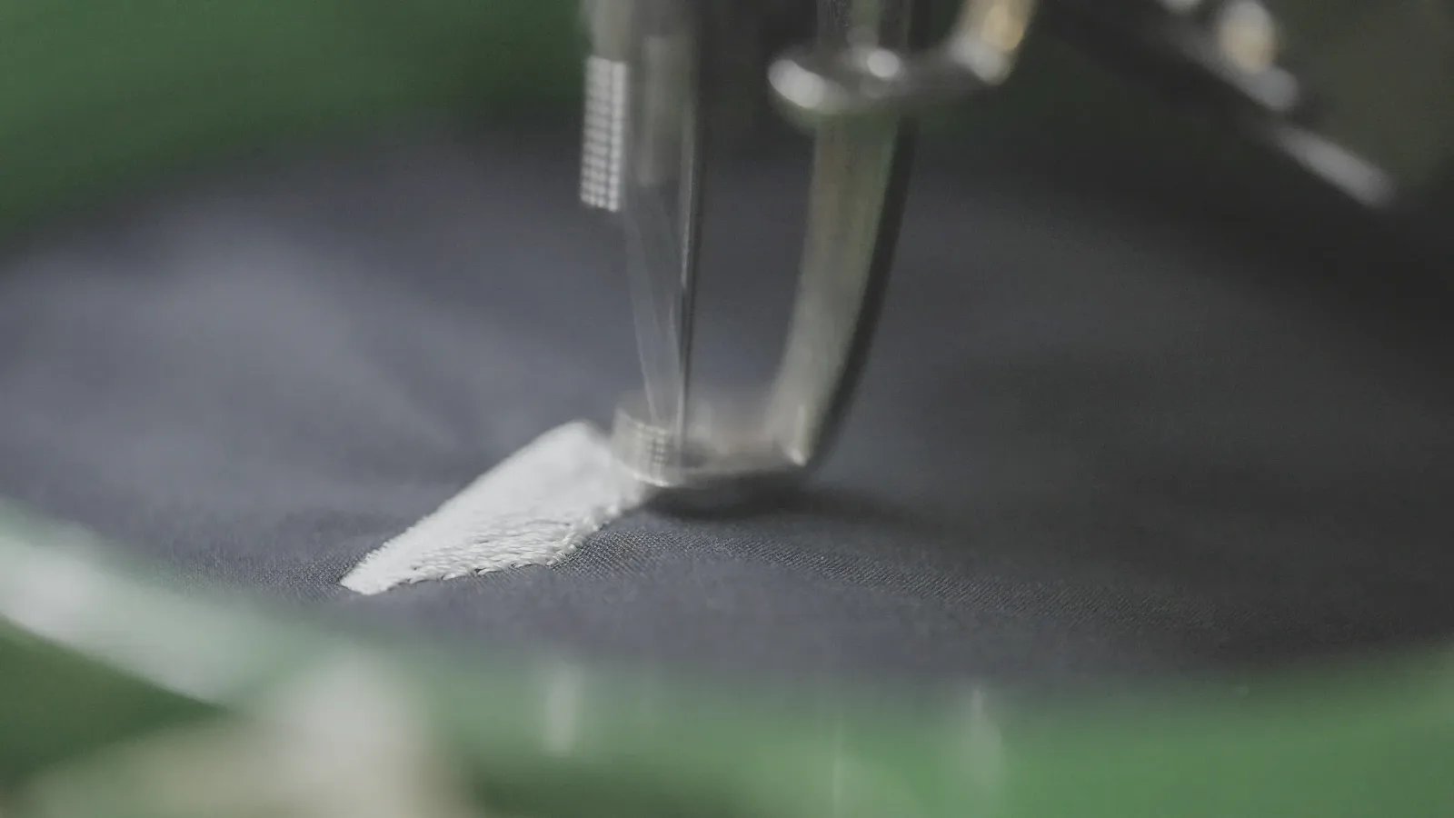 Close-up of an embroidery needle stitching white thread into dark fabric in a hoop