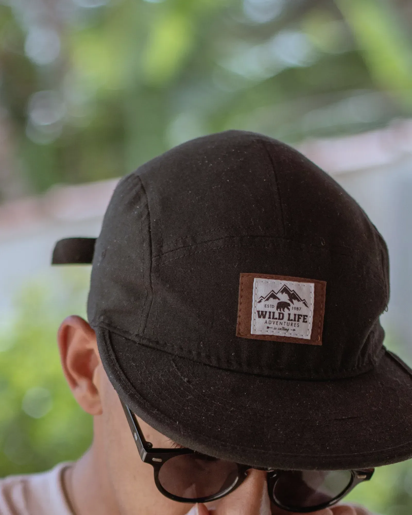 Dark brown five-panel cap with a woven patch on the wide front panel and a flat brim