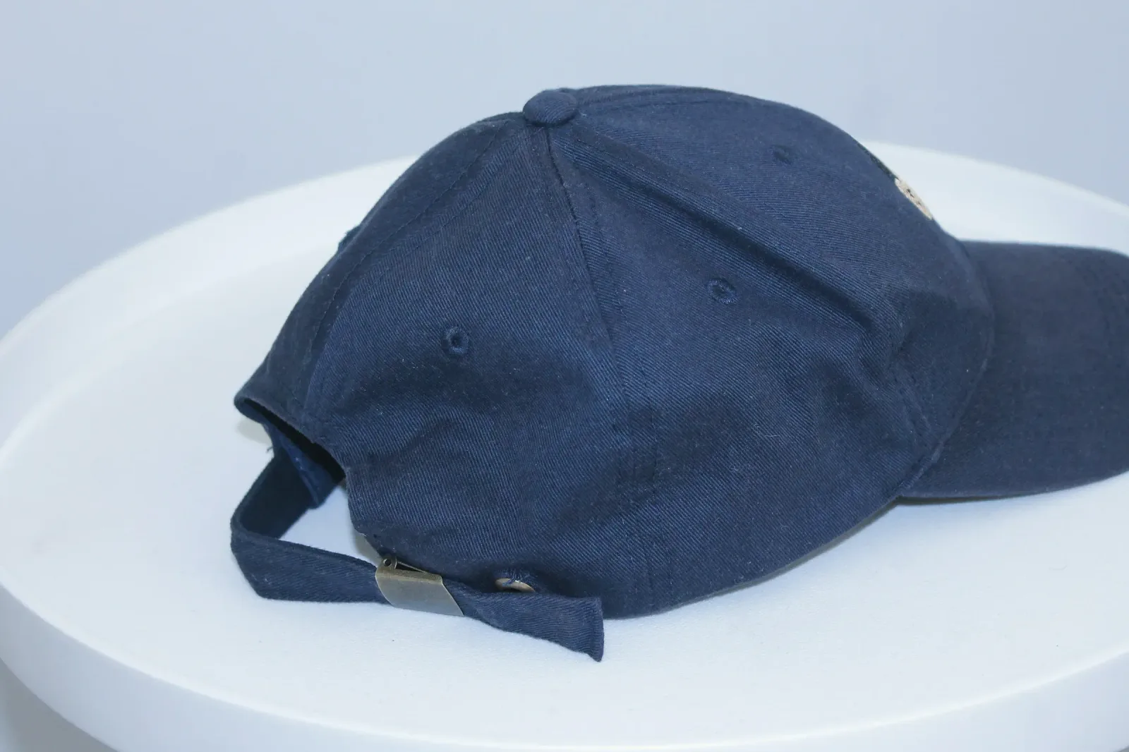 Navyblaue Cap aus Baumwoll-Twill schräg von hinten: sechs Panels, Ösen, bezogener Knopf und Riemen mit Metallschieber