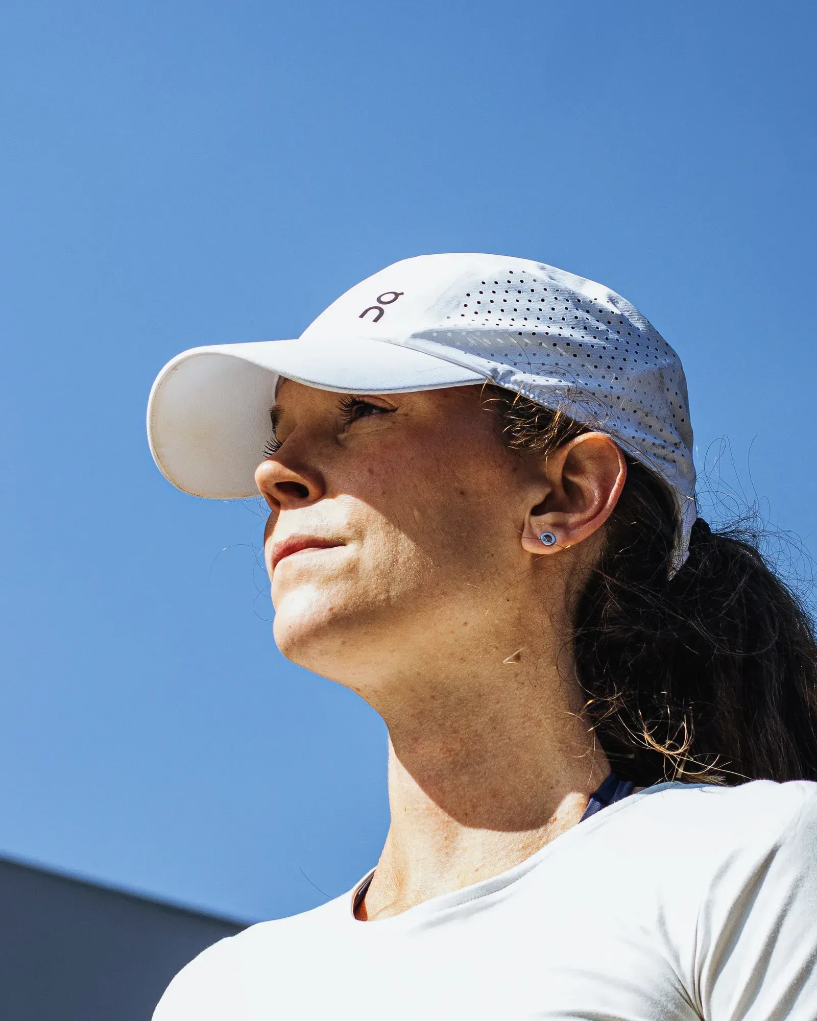 Sportlerin mit einer weißen, leichten Laufcap mit laserperforierten Seitenpanels vor blauem Himmel