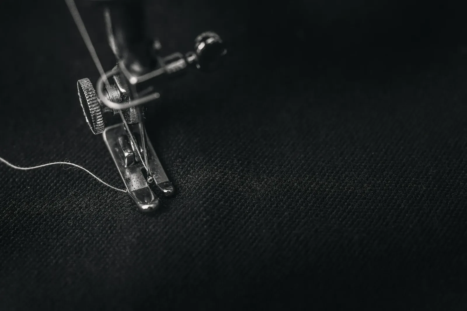 Sewing machine presser foot and needle on dark woven fabric